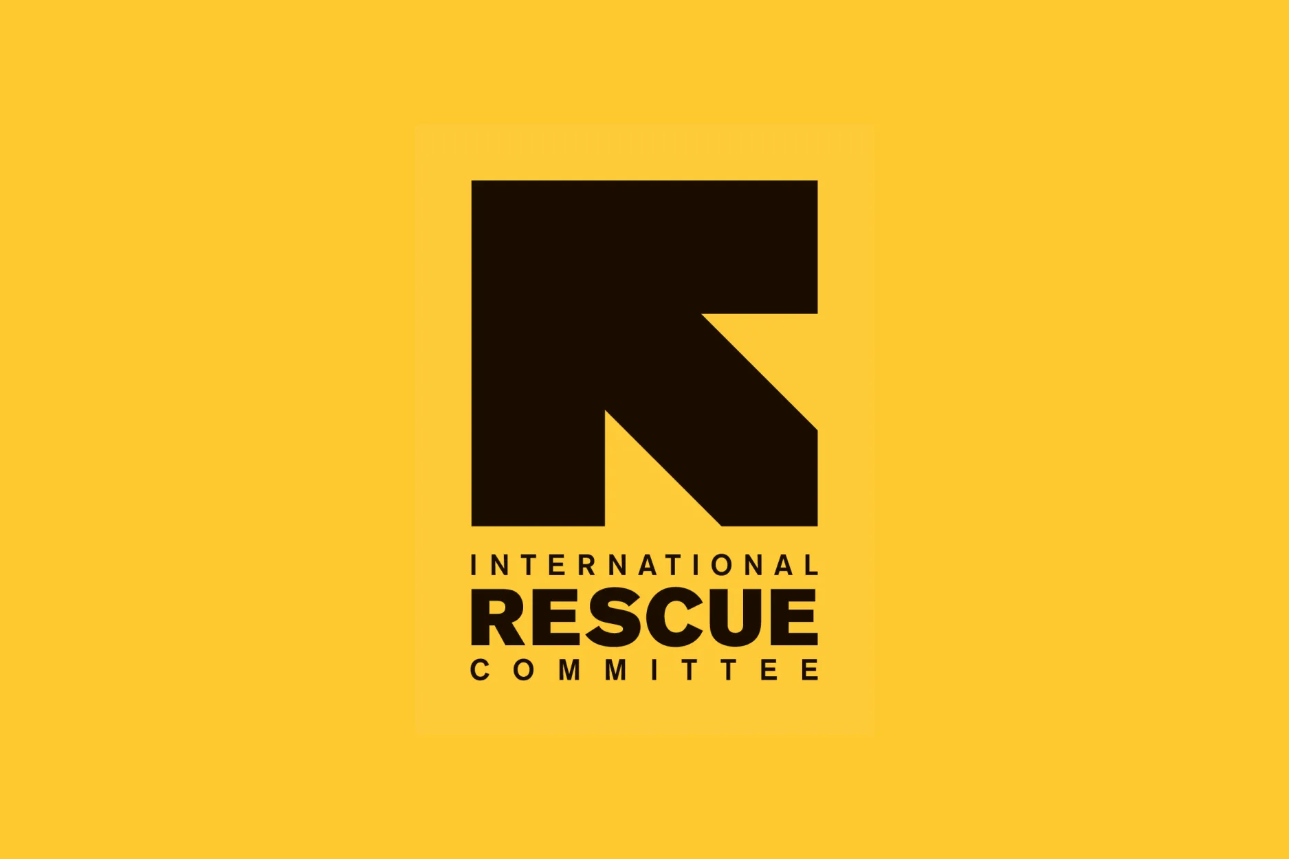 The International Rescue Committee Logo centered on a bright yellow background. The logo contains an arrow pointing upwards and to the left with the text International Rescue Committee below.